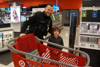 officer smiles with child in front in the target electronics section with a cart filled with a minecraft toy 