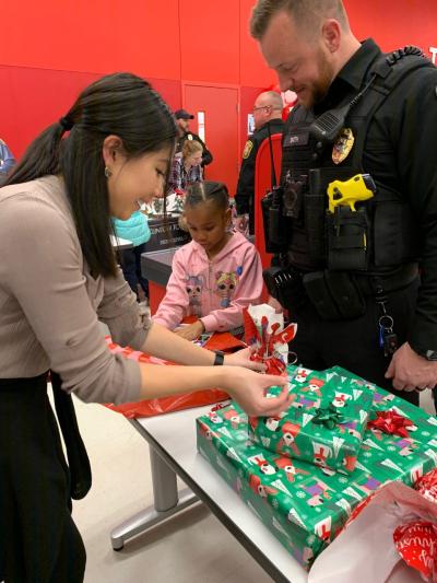 target store employee helps wrap present at wrapping station with child and officer